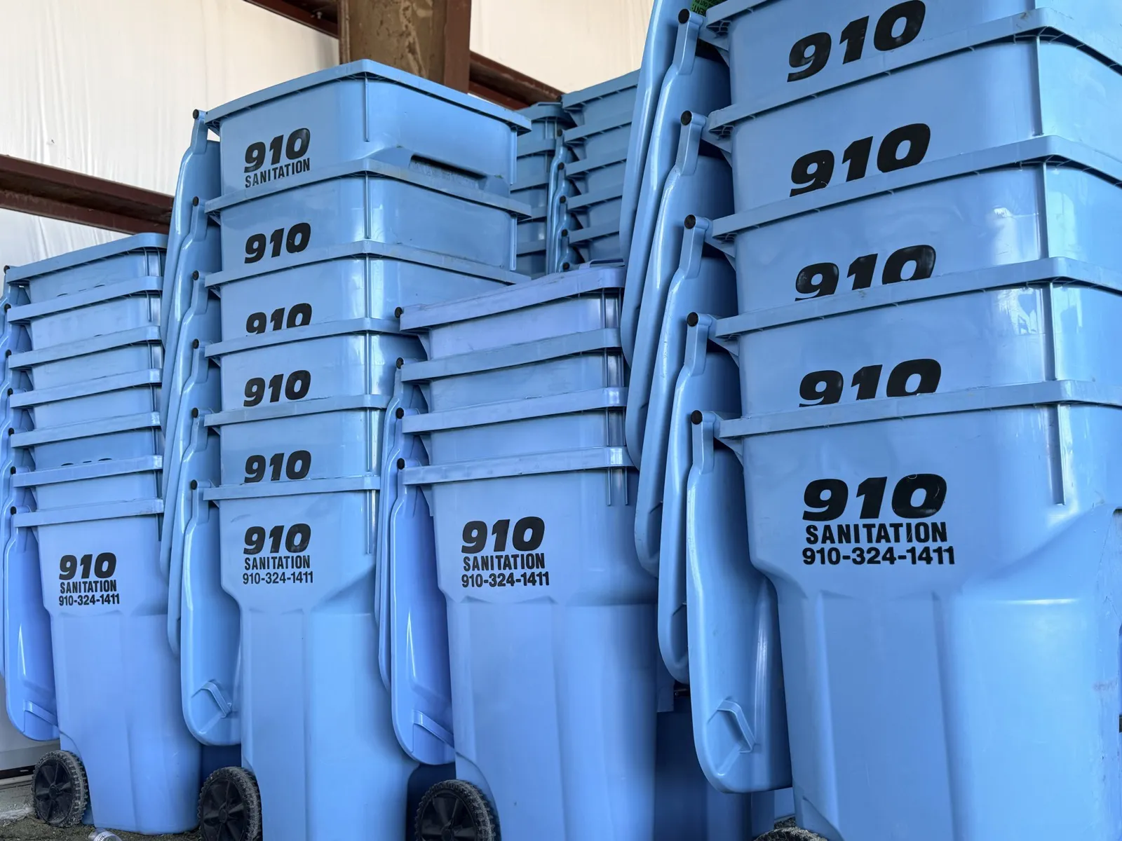 910 Sanitation branded blue trash cans stacked in the warehouse